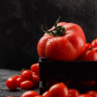 Chilly tomatoes in a wooden box on grey and dark background, side view.
